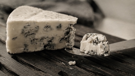 A wedge of Roquefort cheese and a knife on a wooden board